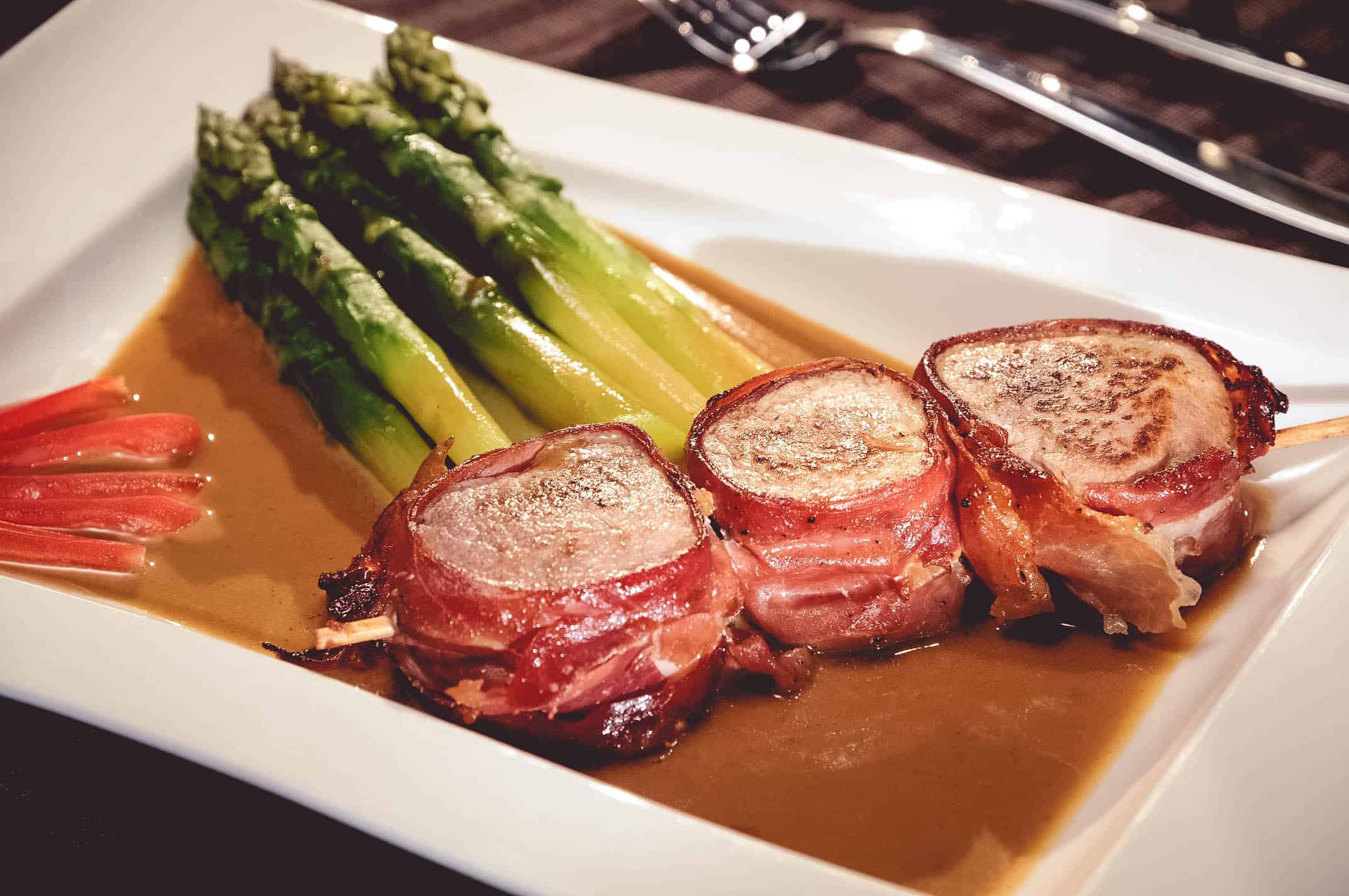 Brochette de filet de porc enrobé de jambon, fricassée d’asperges et jus de veau